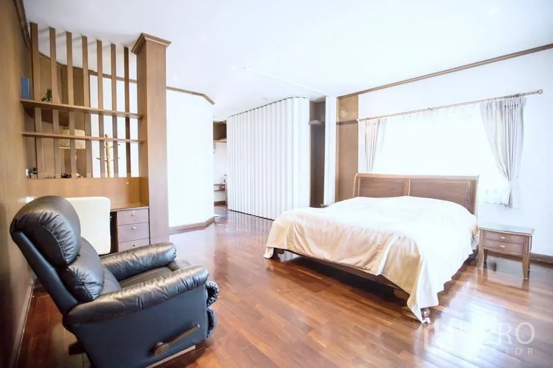 บ้าน ขายในLat Krabang, Bangkok - ห้องนอนหลักกว้าง พื้นไม้ เตียงใหญ่ เก้าอี้เอน และชั้นแบ่งสัดส่วน