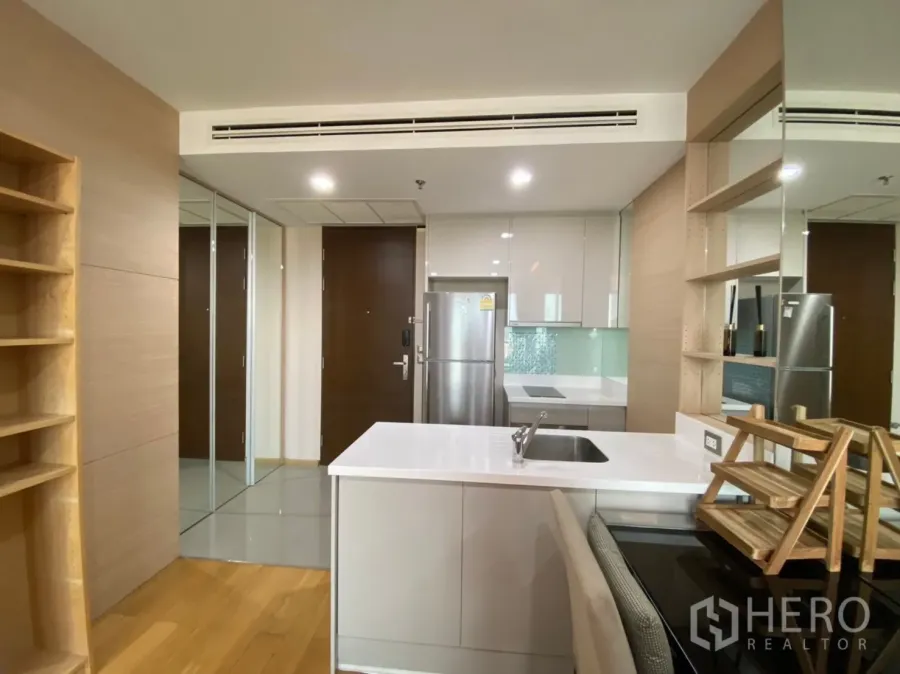 Condominium for rent in Ratchathewi, Bangkok - Modern compact kitchen with white island, built-in shelves, mirrored doors and stainless-steel fridge in a Bangkok condo.