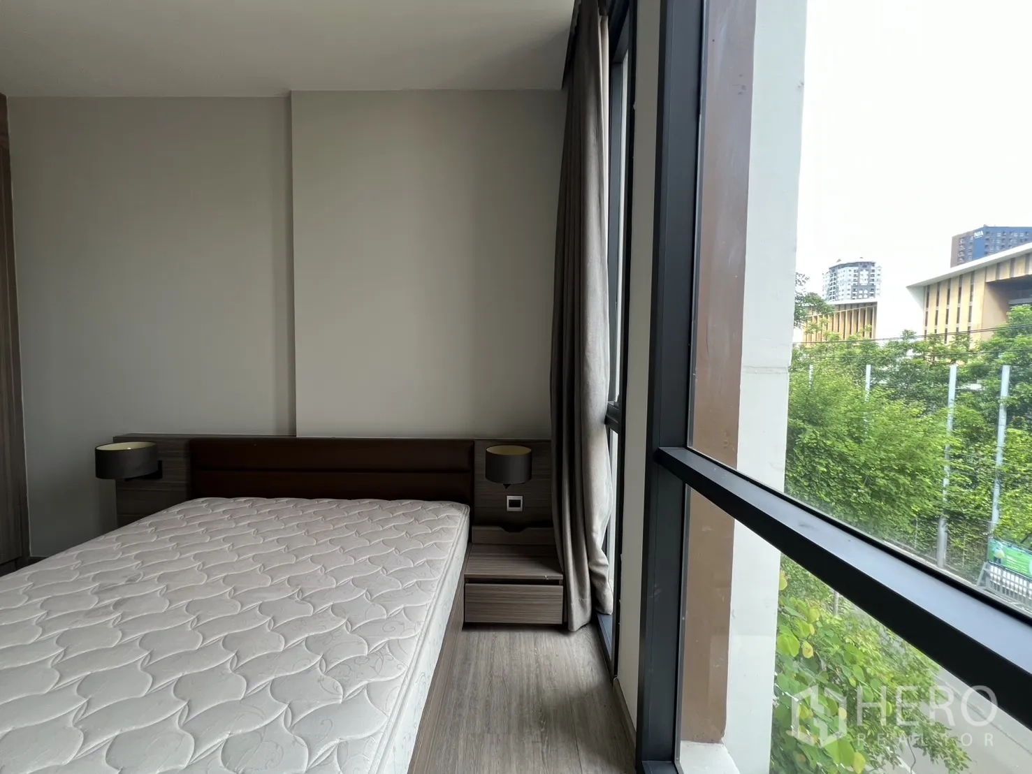 Condominium for rent in Watthana, Bangkok - Bedroom corner with tall windows and bedside tables overlooking trees.