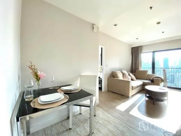 Condominium for rent in Khlong Toei, Bangkok - Bright dining nook for two beside a cozy living room and balcony with city view.