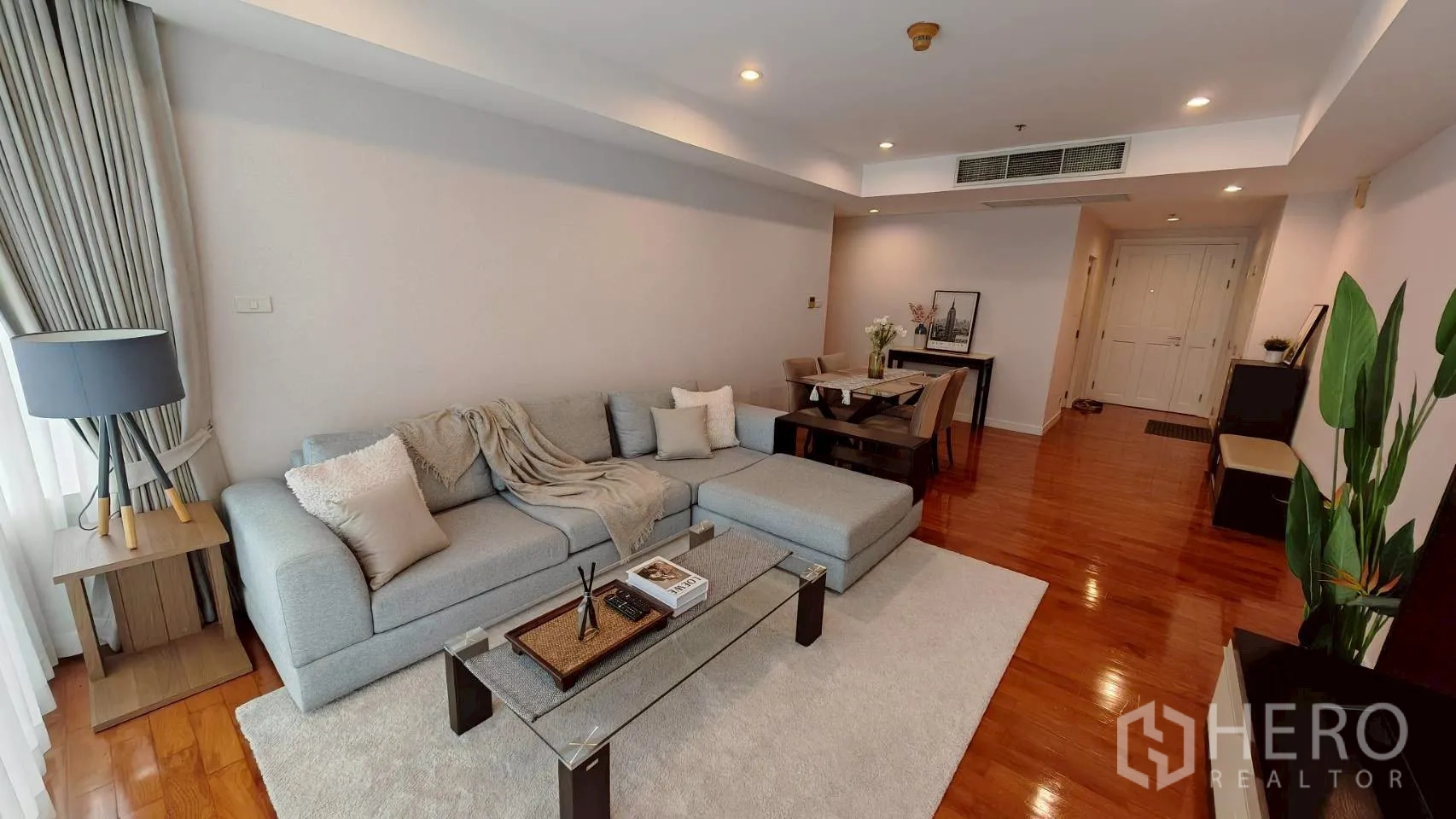 Condominium for rent in Khlong Toei, Bangkok - Another view of the living area with L-shaped sofa and dining table on wooden floors.
