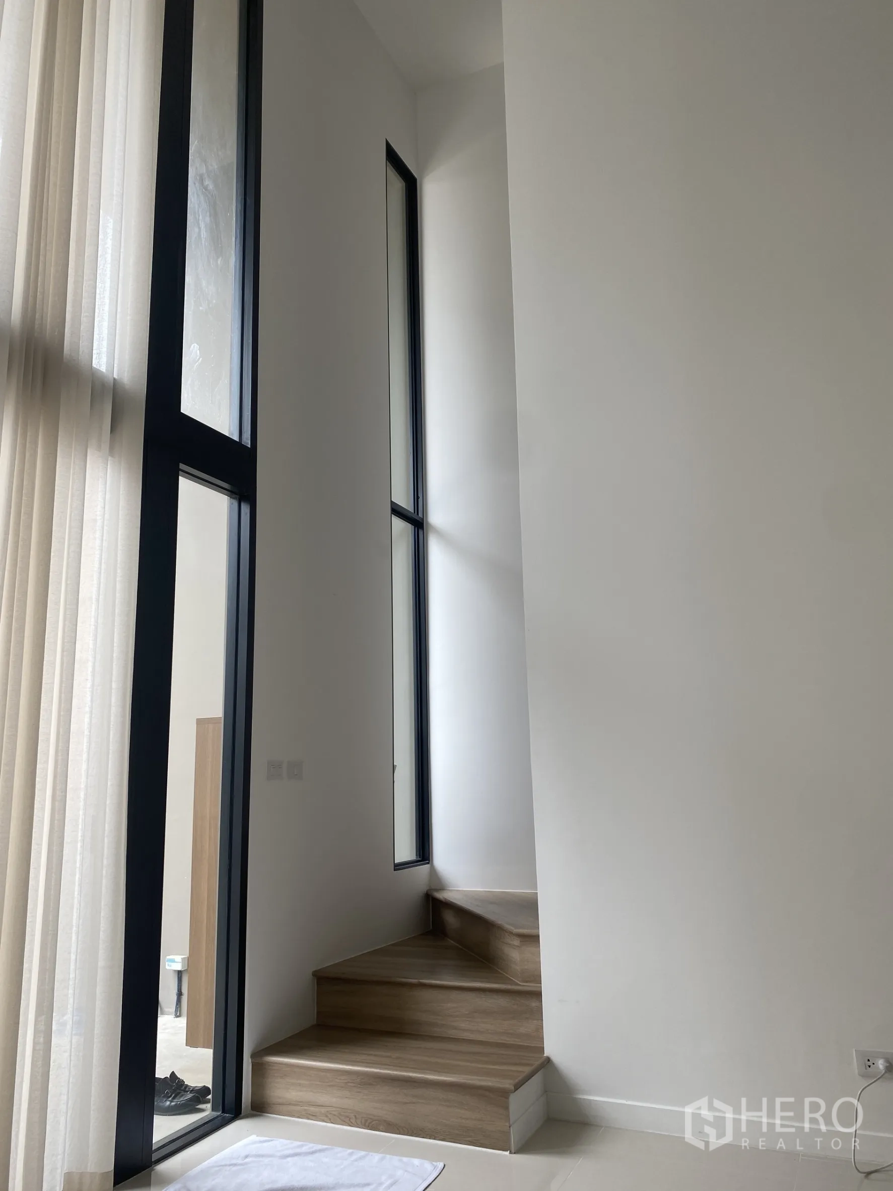 Townhouse for rent or sale in Bang Khae, Bangkok - Wooden staircase beside tall narrow windows and sheer curtains