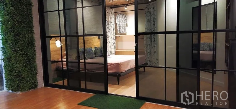 公寓 出售在Watthana, Bangkok - 卧室以黑色金属框玻璃隔断，木质元素与柔和灯光。