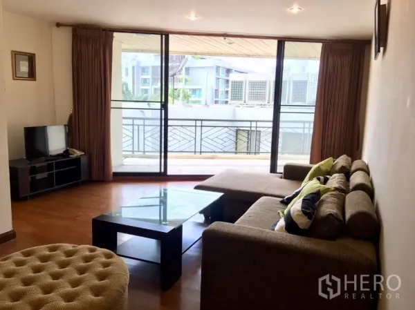 Condominium for rent or sale in Watthana, Bangkok - Bright living room with L-shaped sofa, glass coffee table and balcony sliding doors.