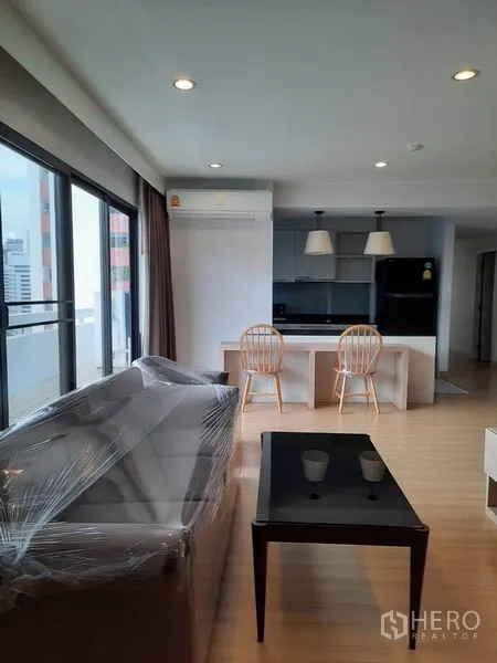 公寓 出租在Watthana, Bangkok - 明亮的客餐一体空间，落地窗、沙发与厨房中岛，近Asok的素坤逸公寓。