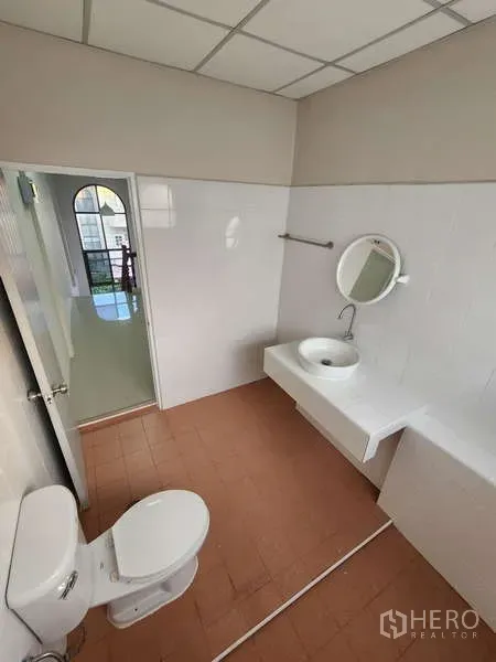 Townhouse for rent in Wang Thonglang, Bangkok - Bright bathroom with white wall tiles, round mirror, sink and toilet.