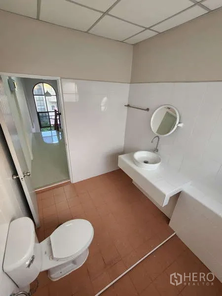 Townhouse for rent in Wang Thonglang, Bangkok - Bright bathroom with white wall tiles, round mirror, sink and toilet.