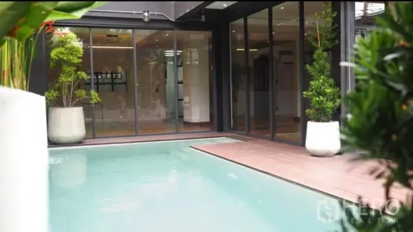 Home Office for rent or sale in Khlong Toei, Bangkok - Courtyard swimming pool beside sliding glass doors and a wooden deck with potted tropical plants.