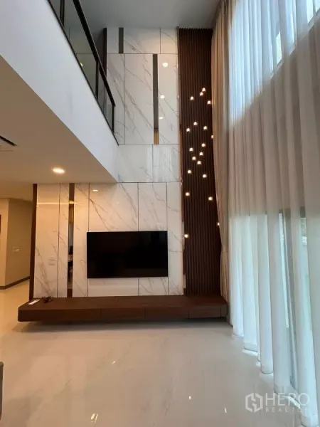 Detached House for rent in Bang Phli, Samut Prakan - Double-height living room with marble feature wall, wall-mounted TV, sheer curtains, and pendant lights.