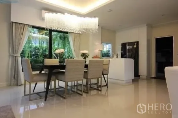 Detached House for rent or sale in Prawet, Bangkok - Dining area beneath a crystal chandelier beside a modern pantry kitchen with sliding glass to greenery.