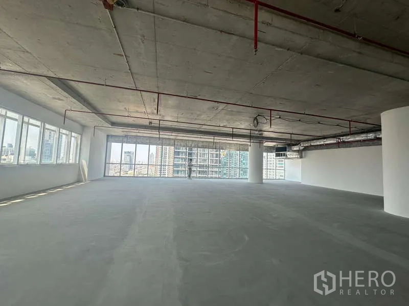 Office Space for rent in Sathon, Bangkok - Open-plan office space with concrete floors and full-height glazing looking toward the Bangkok skyline near BTS Saint Louis.