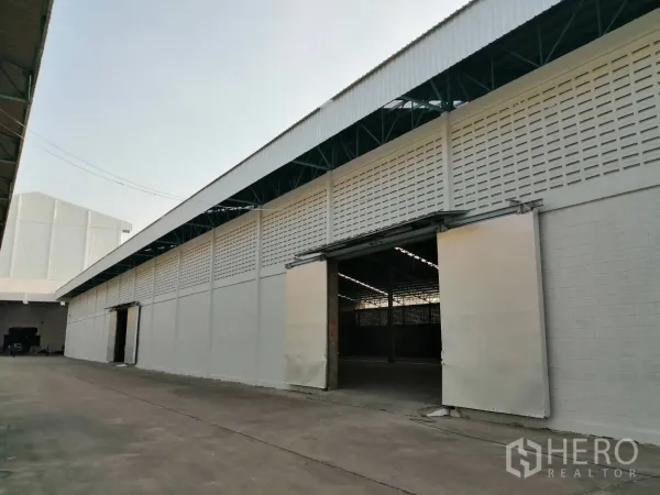 货栈 出租在Mueang Pathum Thani, Pathum Thani - 仓库长立面，推拉门敞开，带有覆盖的装卸通道，园区环境整洁。