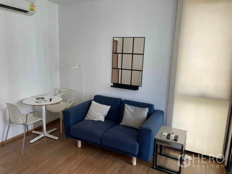 Condominium for sale in Watthana, Bangkok - Cozy corner with a blue two-seater sofa, side table, and small dining set by the window.