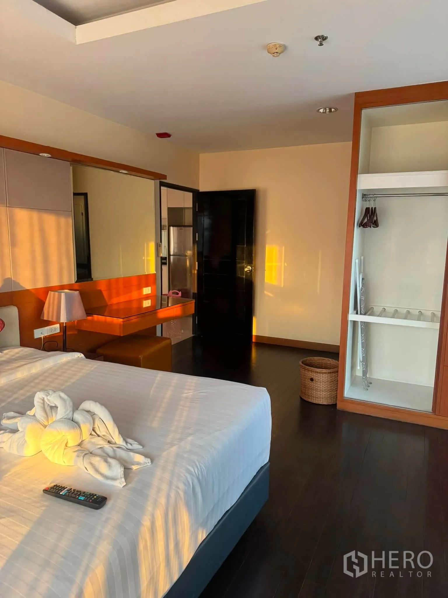 Condominium for rent in Khlong Toei, Bangkok - Bedroom with dark floors, large mirror, open wardrobe, and a dressing table in warm wood tones.