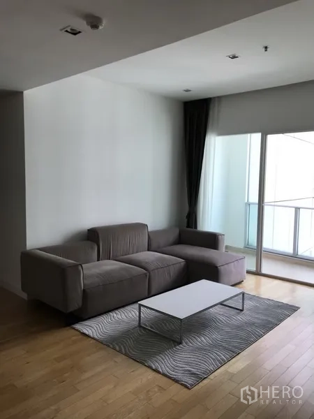 คอนโด ให้เช่าในKhlong Toei, Bangkok - ห้องนั่งเล่นคอนโดย่านสุขุมวิทสว่าง โปร่ง โซฟาแอลสีเทา โต๊ะกลางขาว พรม และทางออกสู่ระเบียง