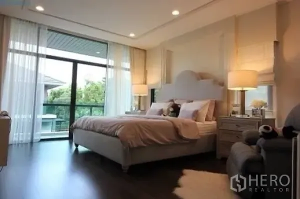 Detached House for rent or sale in Prawet, Bangkok - Master bedroom with large bed, balcony access through full-height glass, and warm wood flooring.