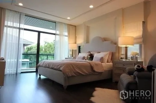 Detached House for rent or sale in Prawet, Bangkok - Master bedroom with large bed, balcony access through full-height glass, and warm wood flooring.