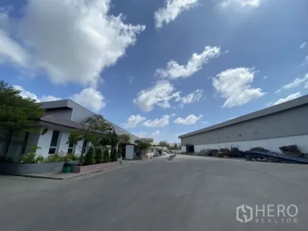 Warehouse for rent in Mueang Samut Sakhon, Samut Sakhon - Wide driveway between large warehouse buildings under a bright blue sky.