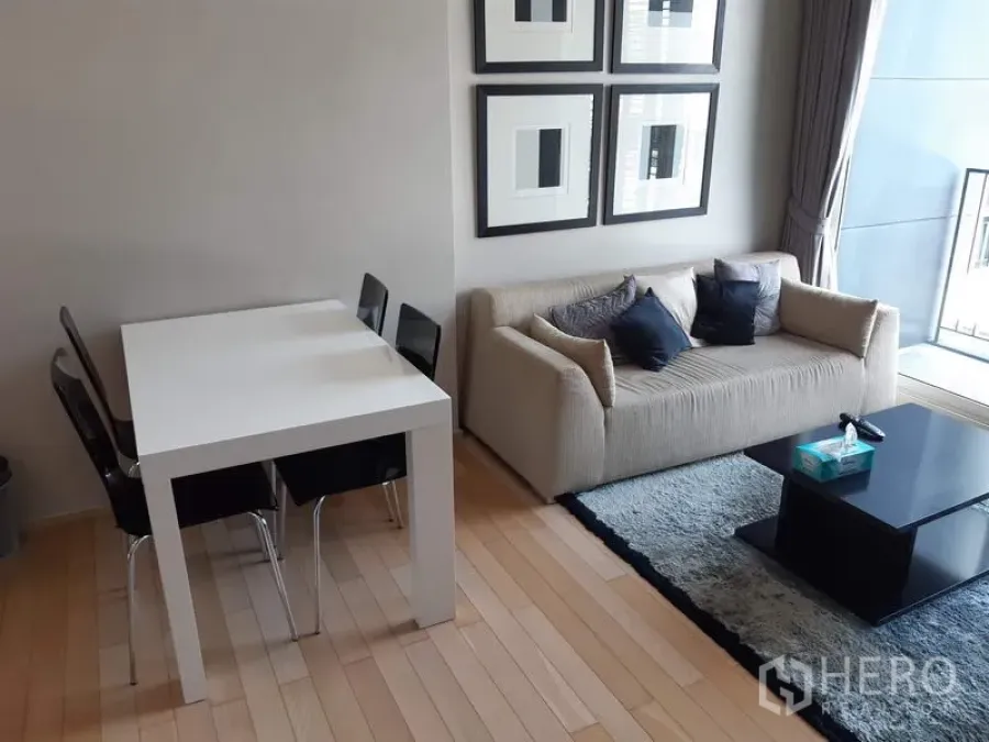 Condominium for rent in Khlong Toei, Bangkok - Cozy lounge with cream sofa, four-seat white dining table and balcony access on light wood flooring.