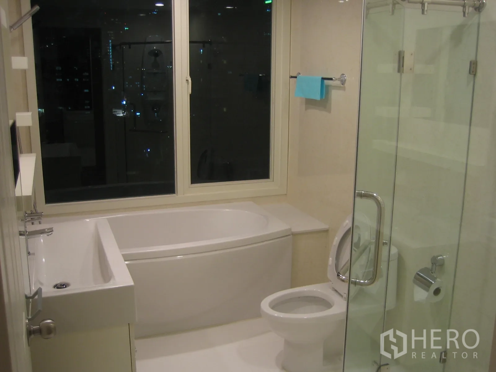 Condominium for rent or sale in Watthana, Bangkok - Modern bathroom featuring a bathtub, glass-enclosed shower, toilet, and a window with a night view.