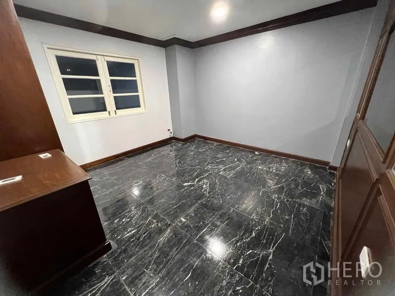 Detached House for sale in Bang Na, Bangkok - Bedroom with glossy black marble floor and custom wooden storage and window.