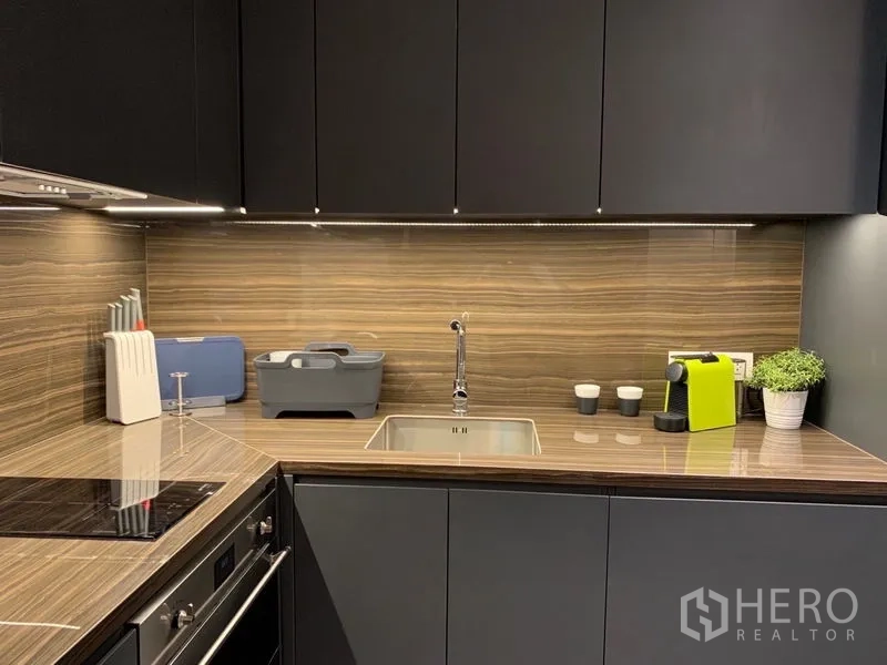 公寓 出租在Bang Rak, Bangkok - 厨房台面与木纹挡板、水槽和咖啡机。