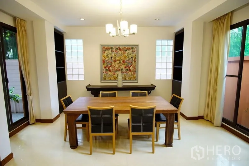Townhouse for rent in Watthana, Bangkok - Dining room with six-seat wooden table, chandelier, and windows on both sides.