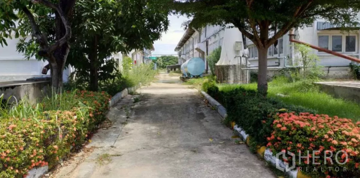 Factory for rent in Bang Pakong, Chachoengsao - Narrow landscaped service lane with shrubs, mature trees and a water tank between factory blocks.
