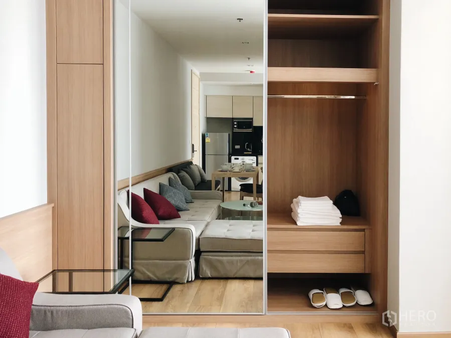 Condominium for rent in Khlong Toei, Bangkok - Bright living area with mirrored wardrobe, open wooden closet and neutral sofa on wood floors.