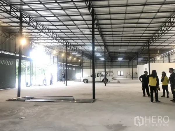 Warehouse for rent in Pathum Thani - Open-plan storage hall with metal trusses, bright lighting, and vehicle access for loading.