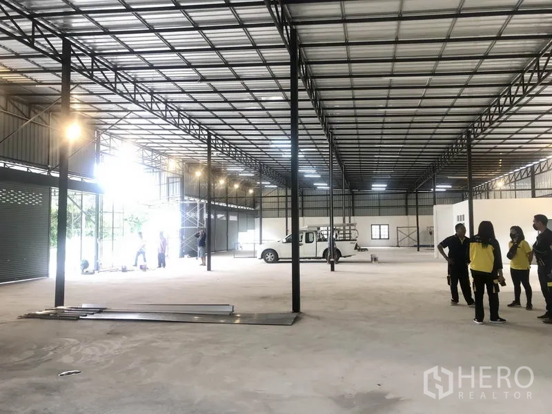 Warehouse for rent in Pathum Thani - Open-plan storage hall with metal trusses, bright lighting, and vehicle access for loading.