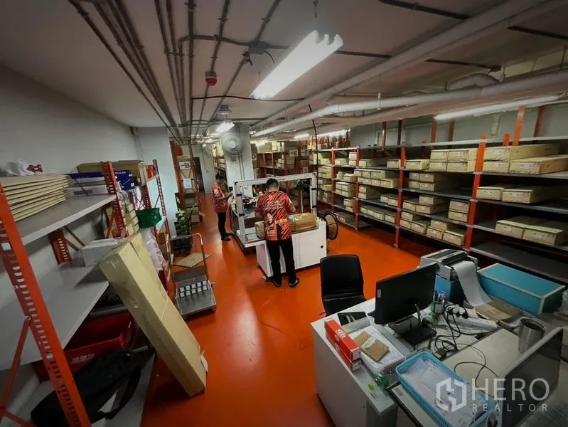 อาคารพาณิชย์ ให้เช่าหรือขายในKhlong Toei, Bangkok - ห้องสต็อกสินค้ามีชั้นวางยาวและโต๊ะแพ็กของ พื้นสีแดง