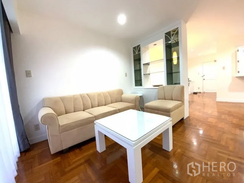 คอนโด ให้เช่าในWatthana, Bangkok - มุมนั่งเล่นอบอุ่นด้วยโซฟารูปตัวแอลสีเบจและโต๊ะกลางสีขาวข้างตู้โชว์