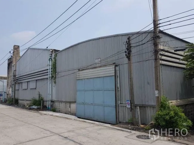 Factory for rent or sale in Bang Phli, Samut Prakan - Row of connected metal warehouses with overhead power lines and dual roller-shutter entrances.