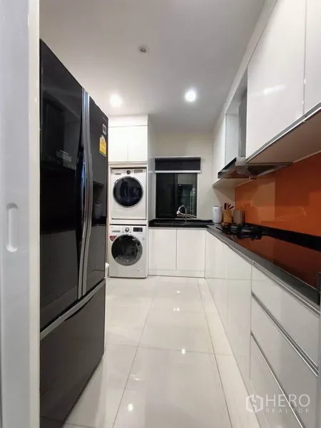 Detached House for rent - Galley kitchen with white cabinets, orange backsplash and stacked washer-dryer.