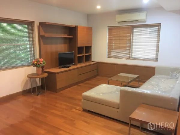 Detached House for rent in Watthana, Bangkok - Bright living room with L-shaped sofa, built-in media cabinet and large windows with blinds.