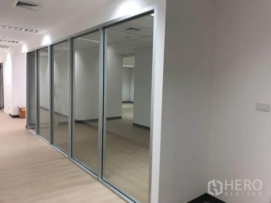 Office Space for rent in Watthana, Bangkok - Glass-walled offices along a corridor with modern lighting in a central Bangkok building.