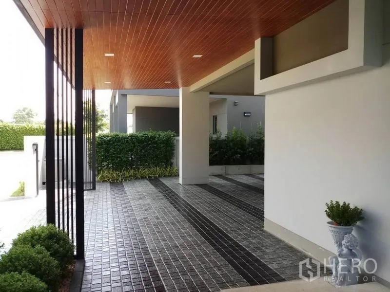 Detached House for sale in Nonthaburi - Covered carport with warm wood ceiling, tiled driveway and green hedges.