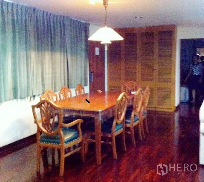 Condominium for rent in Watthana, Bangkok - Eight-seat wooden dining table under a pendant light beside louvered storage.