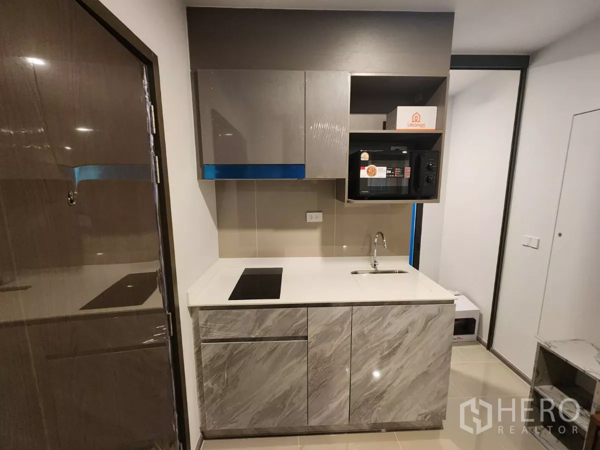 Townhouse for rent in Khlong Toei, Bangkok - Compact kitchen with marble‑look cabinets, induction hob and built‑in microwave.