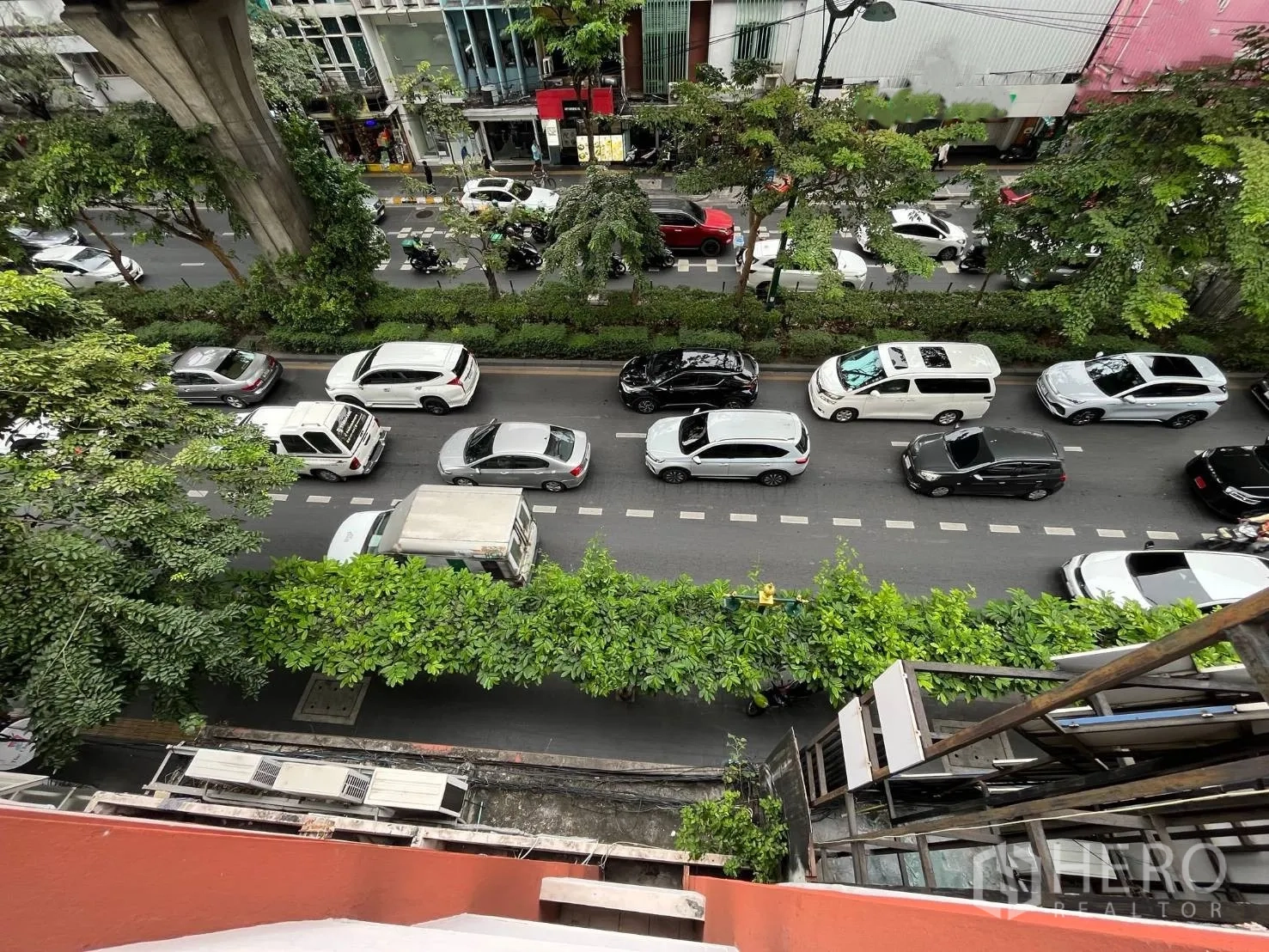 Shophouse for rent in Khlong Toei, Bangkok - Upper-floor view of a busy city road lined with trees and shops.