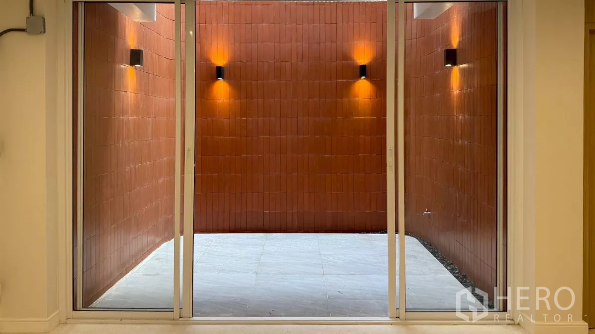 Home Office for rent in Watthana, Bangkok - Internal courtyard with terracotta wall and sconces viewed through sliding glass doors.