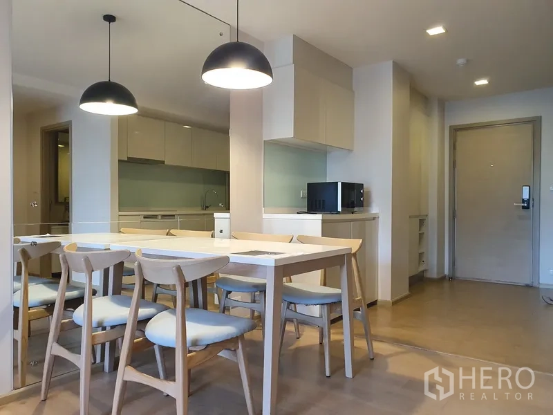 คอนโด ให้เช่าในWatthana, Bangkok - มุมรับประทานอาหารโต๊ะไม้ 6 ที่นั่ง พร้อมโคมไฟแขวนและผนังกระจก ข้างครัวแบบเปิด