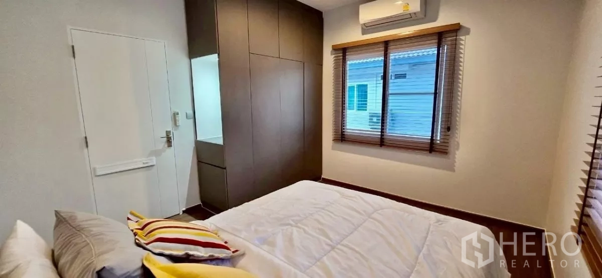 Detached House for rent in Samut Prakan - Compact bedroom with fitted wardrobe, window blinds and AC unit.