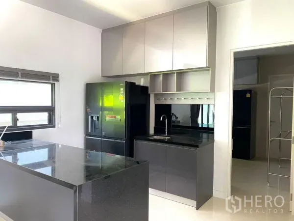 Detached House for sale in Bang Kapi, Bangkok - Contemporary kitchen with black stone island, glossy cabinetry and a large refrigerator.