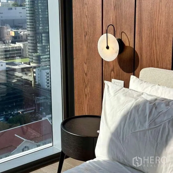 คอนโด ให้เช่าหรือขาย - มุมข้างเตียงผนังไม้ ติดไฟกิ่งทรงกลม และโต๊ะข้างเตียงริมหน้าต่าง