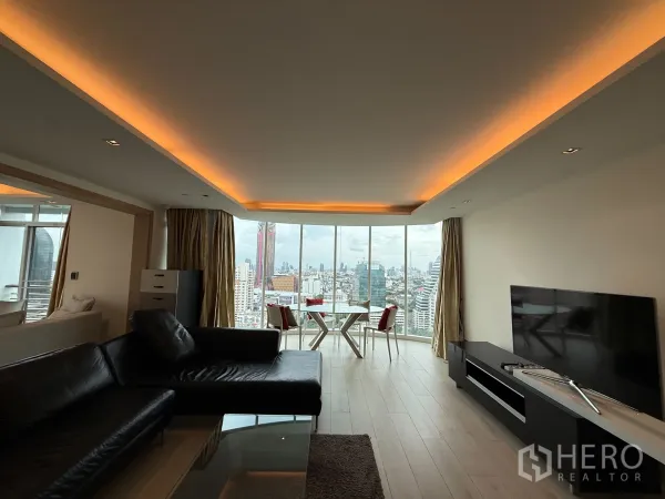 คอนโด ให้เช่าในPhaya Thai, Bangkok - ห้องนั่งเล่นยาวพร้อมไฟซ่อน ฝ้าเพดาน โซฟาเซกชันนอลและทีวี รับวิวเมืองผ่านกระจกบานใหญ่