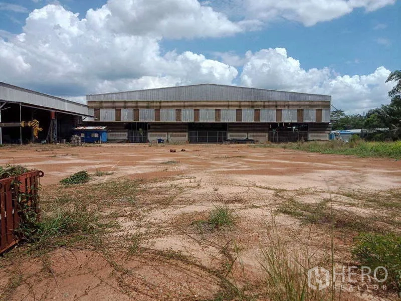 工厂 出售在Chachoengsao - 工业仓库正立面，前方为宽大的红土地作业区。