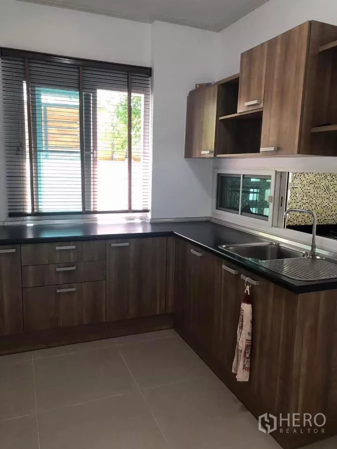 Detached House for rent or sale in Bang Phli, Samut Prakan - L-shaped indoor kitchen with wood cabinetry, black countertops and a window.