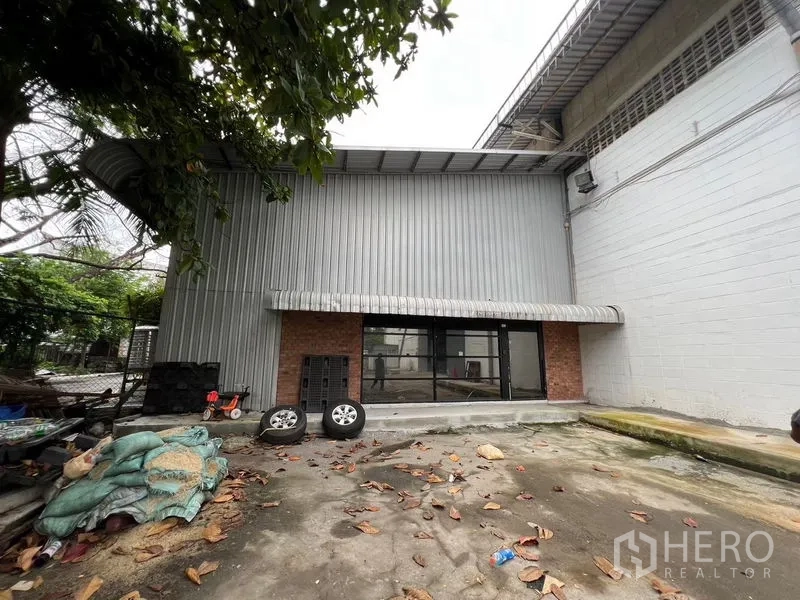 Warehouse for rent in Suan Luang, Bangkok - Suan Luang Bangkok warehouse exterior with corrugated metal cladding, brick accents, glass entry, and a small loading forecourt.